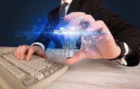 Foto de Empresario sosteniendo bombilla con inscripción ROBOTICS, concepto de tecnología innovadora - Imagen libre de derechos