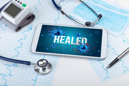 Foto de Tablet PC y herramientas médicas en superficie blanca con inscripción HEALED, concepto pandémico - Imagen libre de derechos
