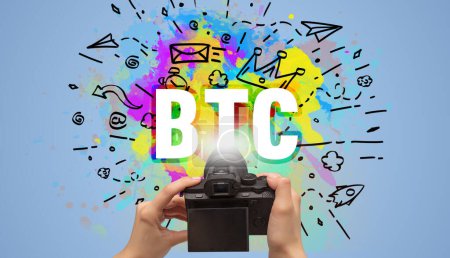 Photo for Close-up of a hand holding digital camera with abstract drawing and BTC inscription - Royalty Free Image