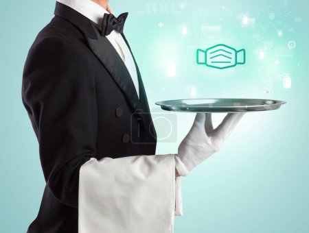 Photo for Handsome young waiter in tuxedo holding tray with mask icons on tray, global healthcare concept - Royalty Free Image