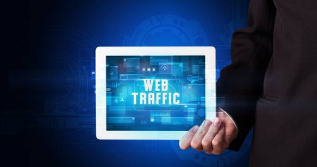 Photo for Young business person working on tablet and shows the digital sign: WEB TRAFFIC - Royalty Free Image