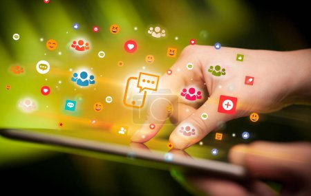 Foto de Primer plano de una mano usando tableta con coloridos iconos de chat de teléfonos inteligentes que salen de ella, concepto de redes sociales - Imagen libre de derechos