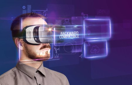 Téléchargez les photos : Homme d'affaires regardant à travers des lunettes de réalité virtuelle avec inscription COMPATIBLE BACKWARD, nouveau concept technologique - en image libre de droit