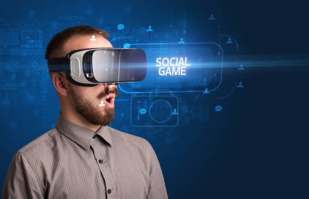 Téléchargez les photos : Homme d'affaires regardant à travers des lunettes de réalité virtuelle avec inscription JEU SOCIAL, concept de réseautage social - en image libre de droit