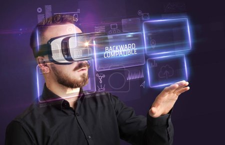 Téléchargez les photos : Homme d'affaires regardant à travers des lunettes de réalité virtuelle avec inscription COMPATIBLE BACKWARD, nouveau concept technologique - en image libre de droit