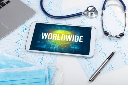 Foto de Tablet PC y herramientas médicas con inscripción WORLDWIDE, concepto de distanciamiento social - Imagen libre de derechos