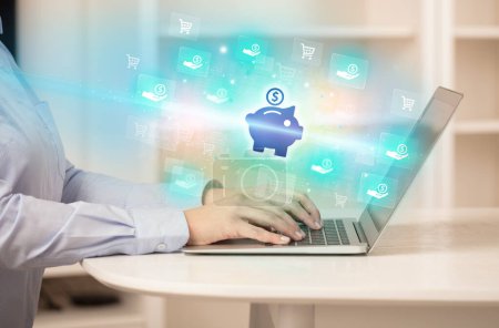 Photo for Businessman working on laptop with piggy bank icons coming out from it, successful business concept - Royalty Free Image