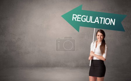 Photo for Young business person in casual holding road sign with REGULATION inscription, business direction concept - Royalty Free Image