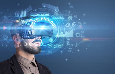 Téléchargez les photos : Homme d'affaires regardant à travers des lunettes de réalité virtuelle avec inscription BIOTECHNOLOGY, concept technologique innovant - en image libre de droit