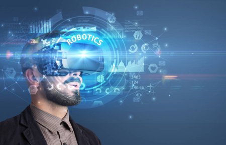 Téléchargez les photos : Homme d'affaires regardant à travers des lunettes de réalité virtuelle avec inscription ROBOTICS, concept technologique innovant - en image libre de droit