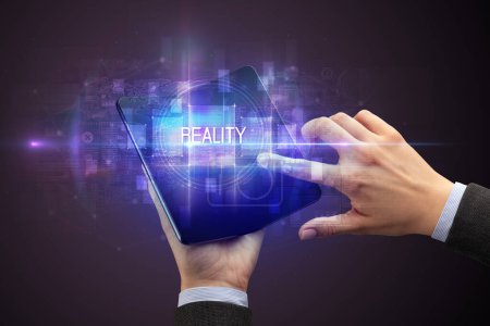 Photo for Businessman holding a foldable smartphone with REALITY inscription, new technology concept - Royalty Free Image