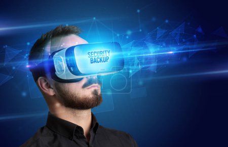 Téléchargez les photos : Homme d'affaires regardant à travers des lunettes de réalité virtuelle avec inscription SECURITY BACKUP, concept de cybersécurité - en image libre de droit