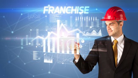 Photo for Handsome businessman with helmet drawing FRANCHISE inscription, architecture business plan concept - Royalty Free Image