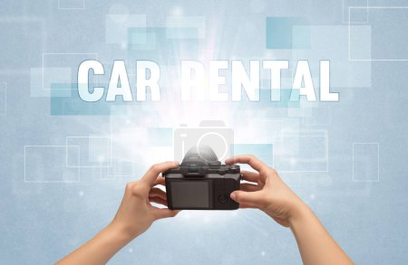 Photo for Close-up of a hand holding digital camera with CAR RENTAL inscription, traveling concept - Royalty Free Image