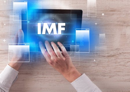 Close-up of a hand holding tablet with IMF abbreviation, modern technology concept