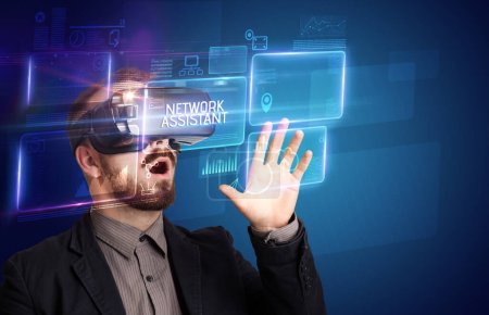 Téléchargez les photos : Homme d'affaires regardant à travers des lunettes de réalité virtuelle avec inscription NETWORK ASSISTANT, nouveau concept technologique - en image libre de droit