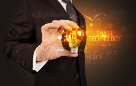 Téléchargez les photos : Homme d'affaires tenant une ampoule avec inscription SMART TECHNOLOGY, concept de technologie d'entreprise - en image libre de droit