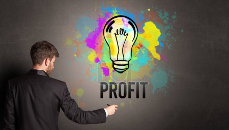 Foto de Hombre de negocios dibujo bombilla de colores con inscripción PROFIT en la pared de hormigón texturizado, nuevo concepto de idea de negocio - Imagen libre de derechos