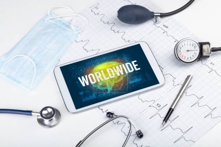 Téléchargez les photos : Tablette pc et outils médicaux avec inscription WORLDWIDE, concept de distanciation sociale - en image libre de droit