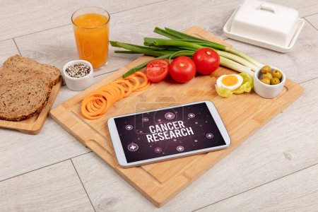 Foto de Concepto de CANCER INVESTIGACIÓN en la tableta PC con alimentos saludables alrededor, vista superior - Imagen libre de derechos
