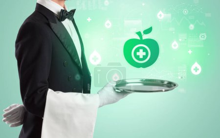 Photo for Handsome young waiter in tuxedo holding tray with healthy apple icons on tray, global healthcare concept - Royalty Free Image