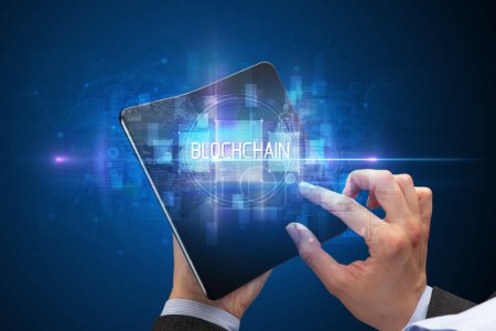 Téléchargez les photos : Homme d'affaires tenant un smartphone pliable avec inscription BLOCKCHAIN, nouveau concept technologique - en image libre de droit