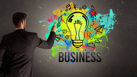 Foto de Hombre de negocios dibujo bombilla de colores con inscripción NEGOCIO en la pared de hormigón texturizado, nuevo concepto de idea de negocio - Imagen libre de derechos