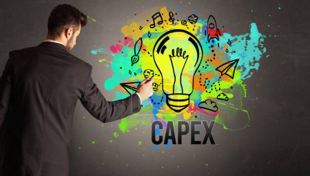 Foto de Hombre de negocios dibujo bombilla de colores con inscripción CAPEX en la pared de hormigón texturizado, nuevo concepto de idea de negocio - Imagen libre de derechos