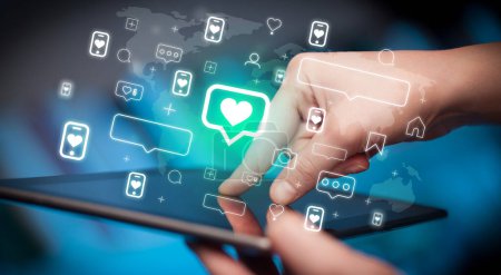 Téléchargez les photos : Gros plan d'une main à l'aide d'une tablette avec bulle vocale avec des icônes cardiaques qui en sortent, concept de médias sociaux - en image libre de droit