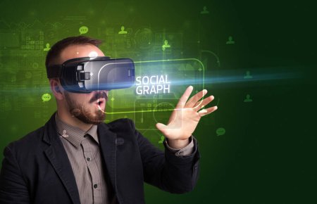 Téléchargez les photos : Homme d'affaires regardant à travers des lunettes de réalité virtuelle avec inscription SOCIAL GRAPH, concept de réseautage social - en image libre de droit
