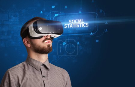Téléchargez les photos : Homme d'affaires regardant à travers des lunettes de réalité virtuelle avec inscription STATISTIQUE SOCIALE, concept de réseautage social - en image libre de droit