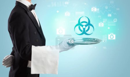 Photo for Handsome young waiter in tuxedo holding tray with biohazard icons on tray, global healthcare concept - Royalty Free Image