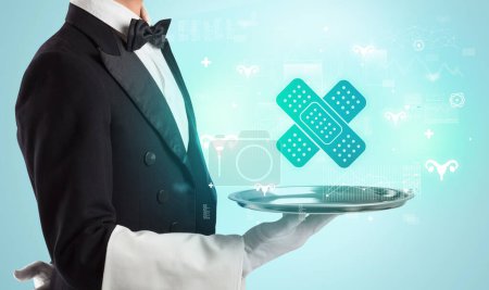 Photo for Handsome young waiter in tuxedo holding tray with bandage icons on tray, global healthcare concept - Royalty Free Image