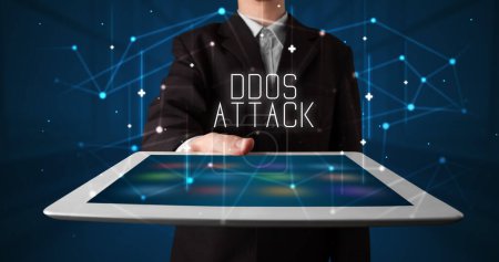 Téléchargez les photos : Jeune homme d'affaires travaillant sur tablette et montre le signe numérique : DDOS ATTACK - en image libre de droit