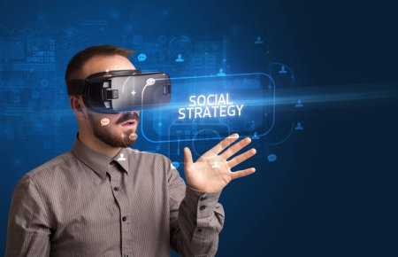 Téléchargez les photos : Homme d'affaires regardant à travers des lunettes de réalité virtuelle avec inscription STRATÉGIE SOCIALE, concept de réseautage social - en image libre de droit