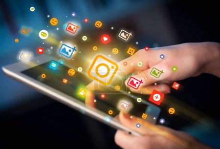 Foto de Primer plano de una mano usando tableta con iconos de cámara de colores que salen de ella, concepto de redes sociales - Imagen libre de derechos