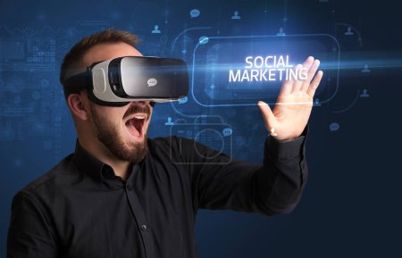 Téléchargez les photos : Homme d'affaires regardant à travers des lunettes de réalité virtuelle avec inscription MARKETING SOCIAL, concept de réseautage social - en image libre de droit
