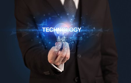 Foto de Empresario sosteniendo bombilla con inscripción TECNOLOGÍA, concepto de tecnología innovadora - Imagen libre de derechos