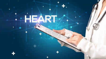 Photo for Doctor fills out medical record with HEART inscription, medical concept - Royalty Free Image