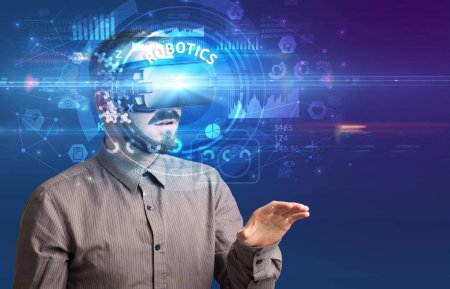 Téléchargez les photos : Homme d'affaires regardant à travers des lunettes de réalité virtuelle avec inscription ROBOTICS, concept technologique innovant - en image libre de droit