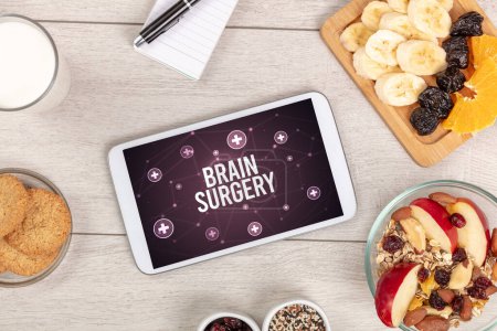 Téléchargez les photos : Chirurgie du cerveau concept en comprimé PC avec des aliments sains autour, vue du dessus - en image libre de droit