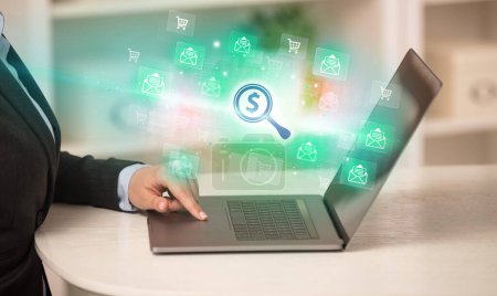 Photo for Businessman working on laptop with magnifying glass with a dollar sign icons coming out from it, successful business concept - Royalty Free Image