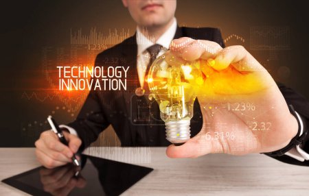 Téléchargez les photos : Homme d'affaires tenant une ampoule avec inscription TECHNOLOGIE INNOVATION, concept de technologie d'entreprise - en image libre de droit