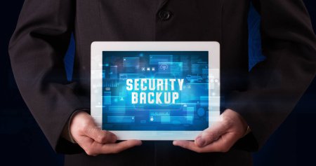 Photo for Young business person working on tablet and shows the digital sign: SECURITY BACKUP - Royalty Free Image