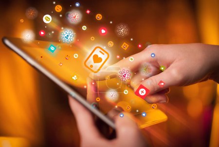 Foto de Primer plano de una mano usando tableta con coloridos teléfonos inteligentes con iconos del corazón que salen de ella, concepto de redes sociales - Imagen libre de derechos
