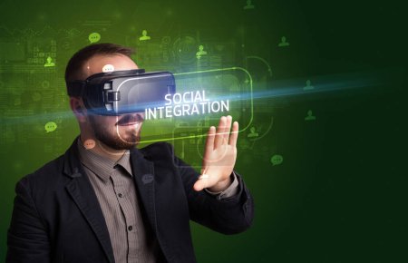 Téléchargez les photos : Homme d'affaires regardant à travers des lunettes de réalité virtuelle avec inscription INTÉGRATION SOCIALE, concept de réseautage social - en image libre de droit