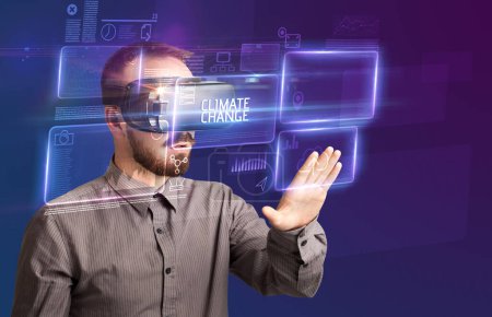 Téléchargez les photos : Homme d'affaires regardant à travers des lunettes de réalité virtuelle avec inscription CLIMATE CHANGE, nouveau concept technologique - en image libre de droit