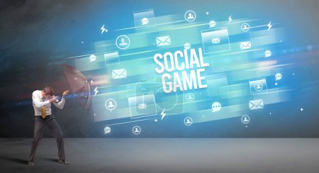 Handsome businessman defending with umbrella from SOCIAL GAME inscription, new age media concept