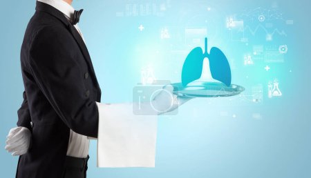 Photo for Handsome young waiter in tuxedo holding tray with lungs icons on tray, global healthcare concept - Royalty Free Image