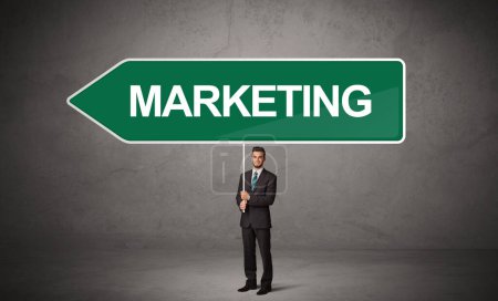 Young business person in casual holding road sign with MARKETING inscription, new business direction concept